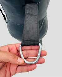 Hand holding a metal D-ring with a strap against a gray background