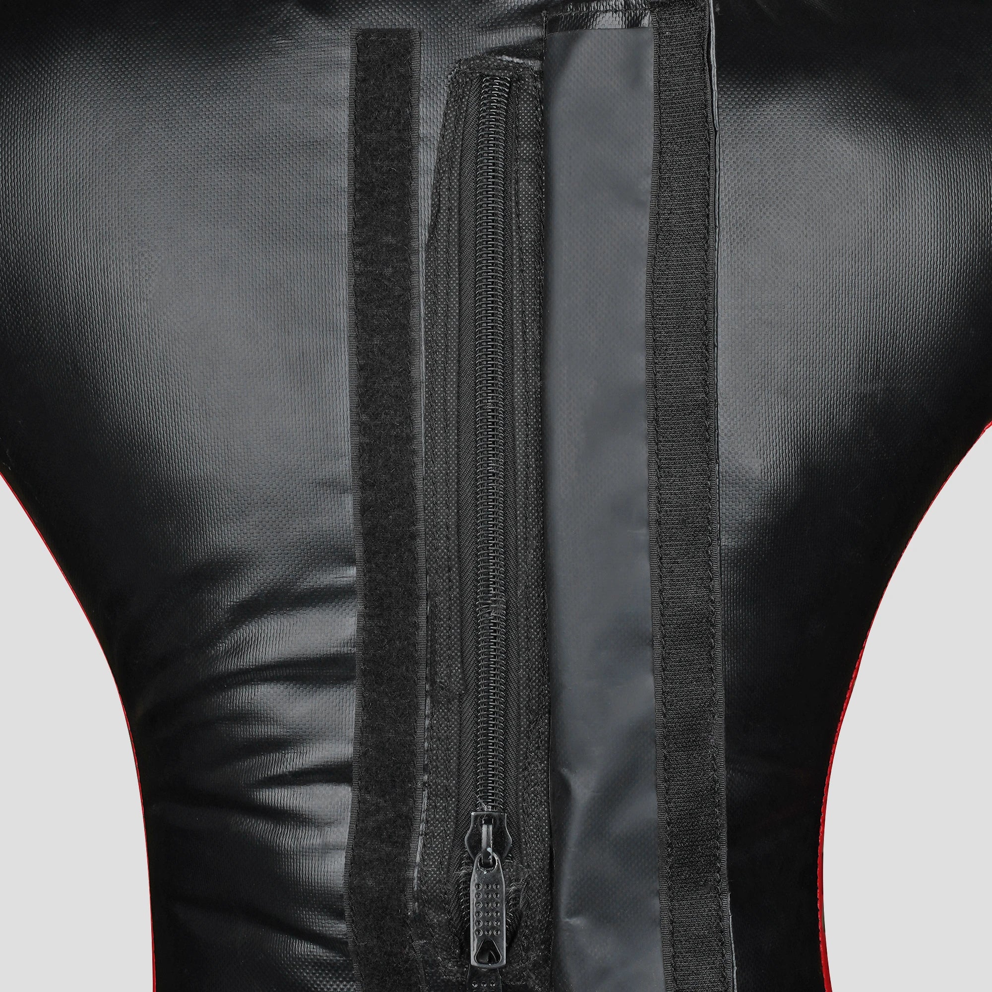 Close-up of the back of a black faux-leather or leather garment, showing a central vertical zipper, hook-and-loop fastening strips, and a thin red piping accent along the sides.