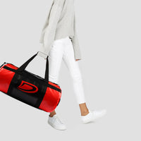 Person holding a red and black duffel bag on a light gray background