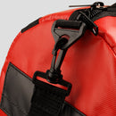 Close-up of a red bag with black straps and zippers on a light gray background