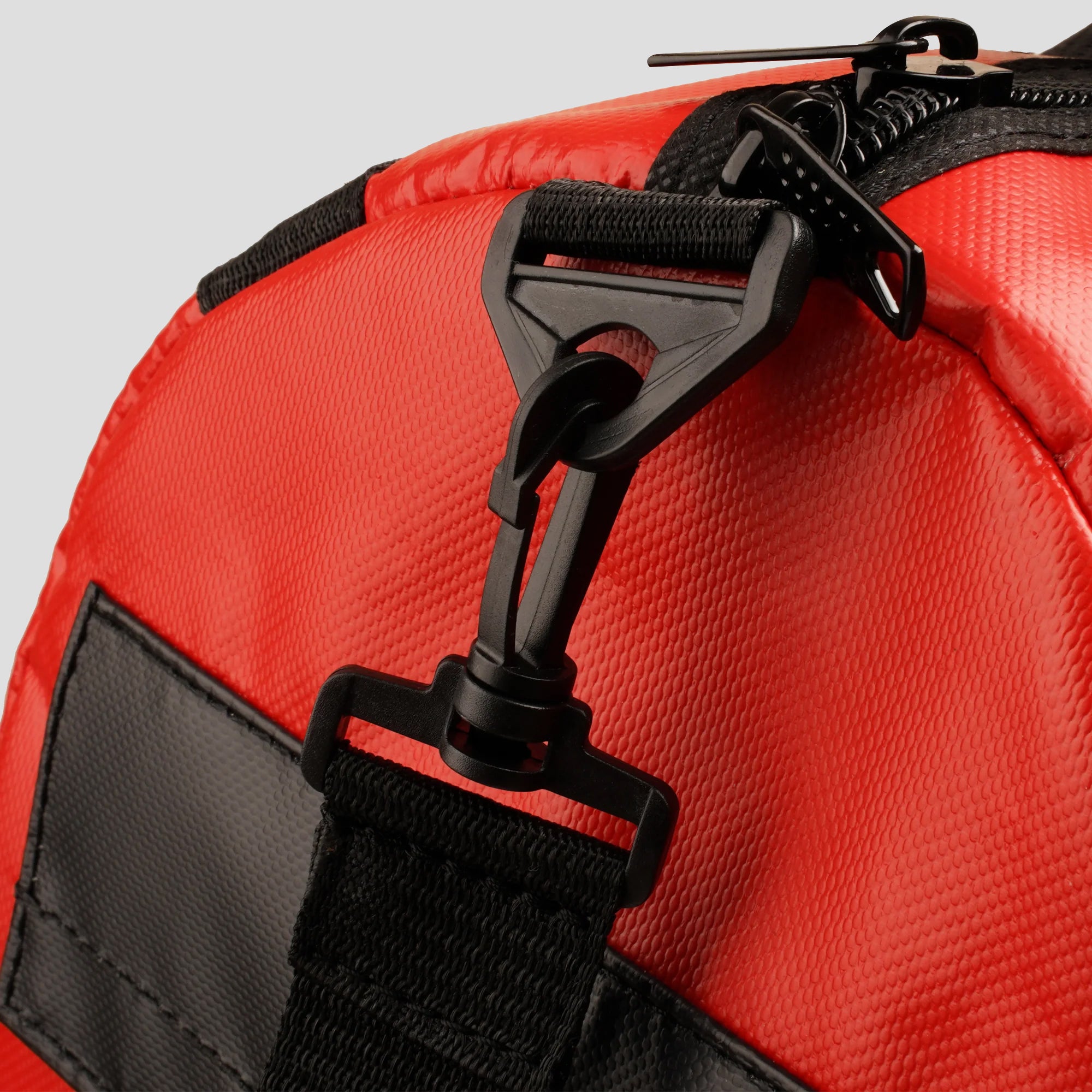 Close-up of a red bag with black straps and zippers on a light gray background