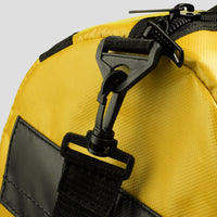 Close-up of a yellow bag with black straps and zipper on a light gray background